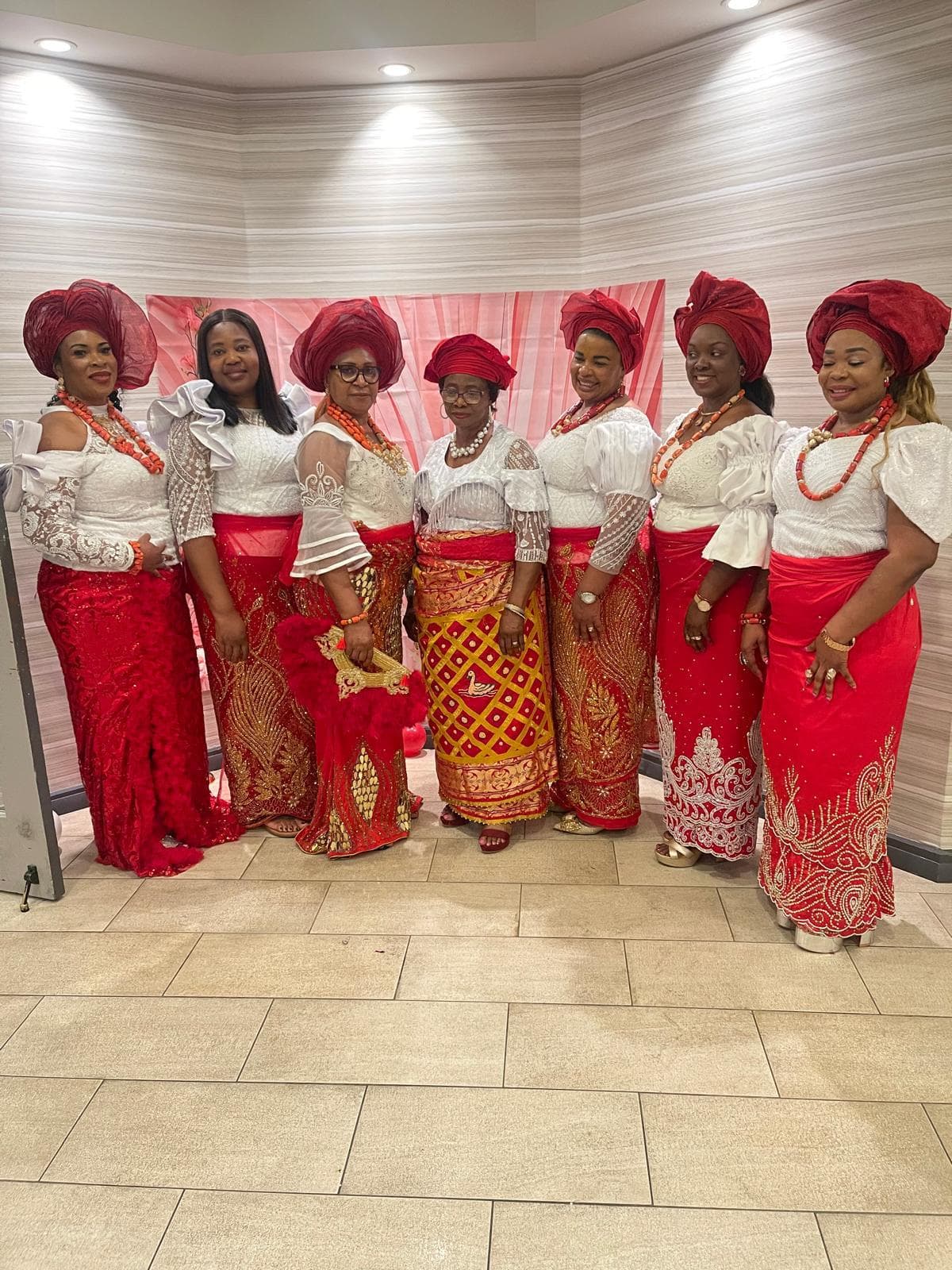Eight Egbu women members in matching red head ties and white lace tops, standing together