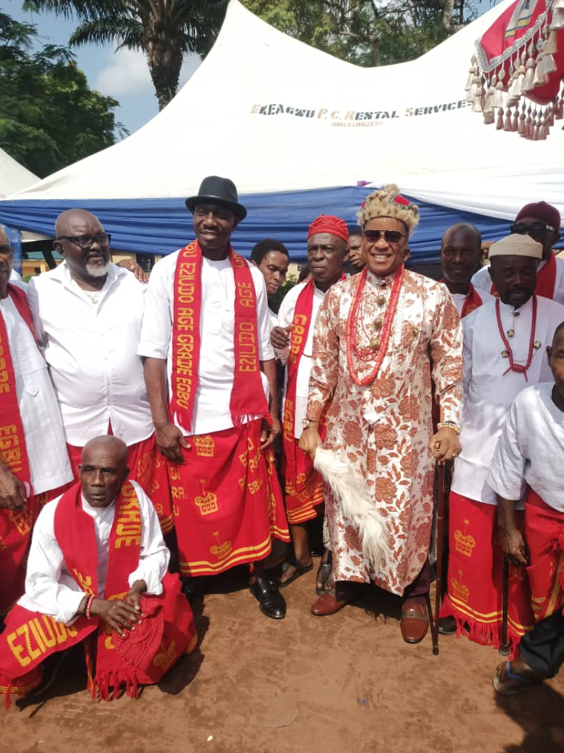 Men in red wrappers and regalia posing together under a tent